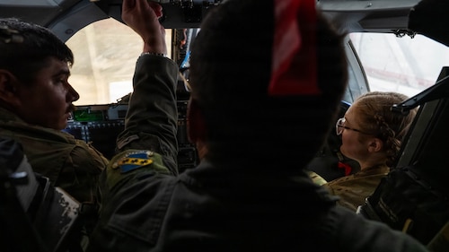 Airmen and civilians stand in a group and receive a brief