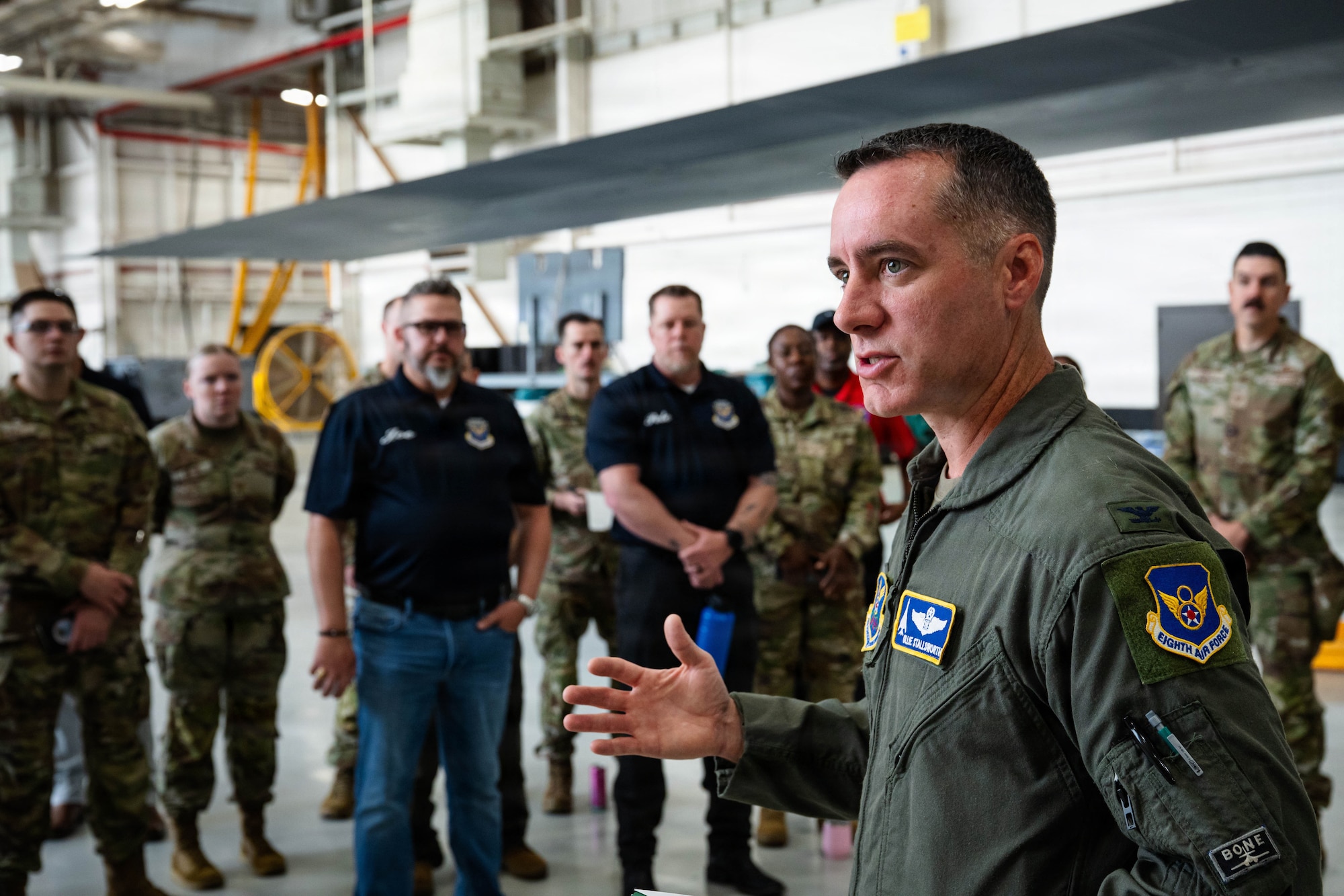 Airmen and civilians stand in a group and receive a brief