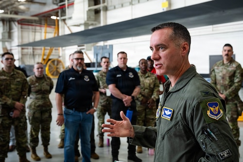 Airmen and civilians stand in a group and receive a brief