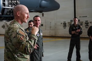 Airmen and civilians stand in a group and receive a brief
