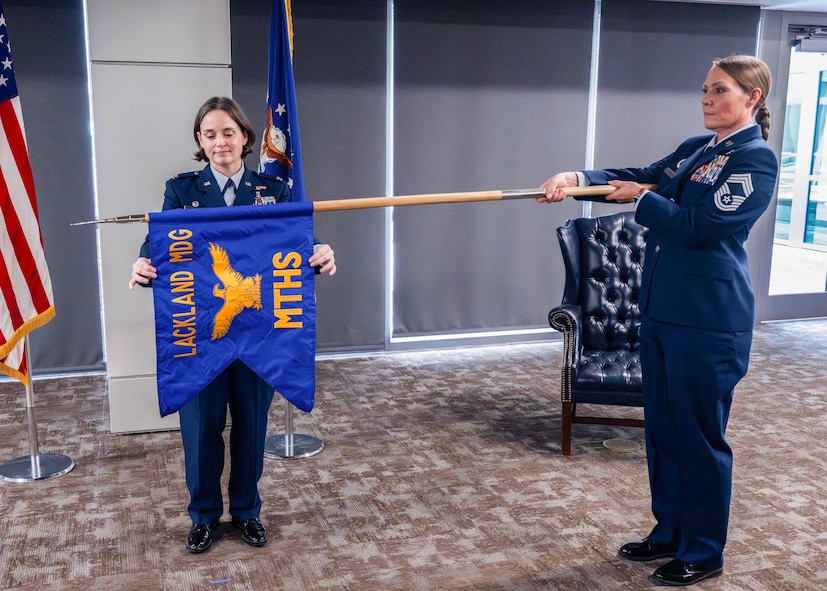 U.S. Air Force Col. Shawn Garcia, commander of the Lackland Medical Group, and Chief Master Sgt. Codi Bowman, senior enlisted leader of the Lackland Mental Health Squadron, unfurl the squadron guidon during the unit's activation ceremony at Wilford Hall Ambulatory Surgical Center, Joint Base San Antonio-Lackland, Texas, June 25, 2026.