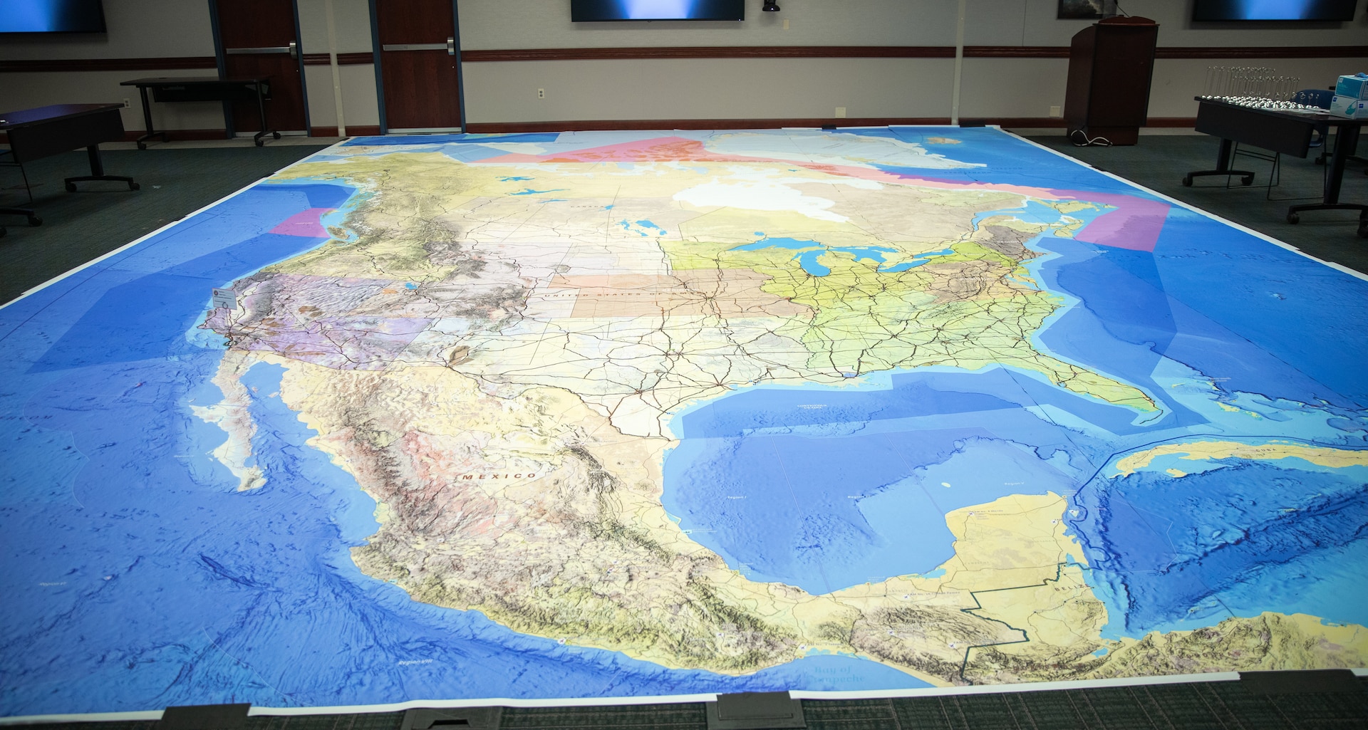 The "Big Atlas Map," or BAM, covers the floor at North American Aerospace Defense Command and U.S. Northern Command headquarters on April 27, 2026. Designed and produced on a compressed timeline by Rich Hanes, an analyst with the National Geospatial-Intelligence Agency, the 25-by-28-foot map details North American strategic seaports, airports, rail lines and interstate highways. It served as the central planning tool for the 2026 Sustainment Rehearsal of Concept (ROC) Drill, enabling logisticians to physically walk through force flow and distribution concepts. (Department of War photo by Blake Macias)