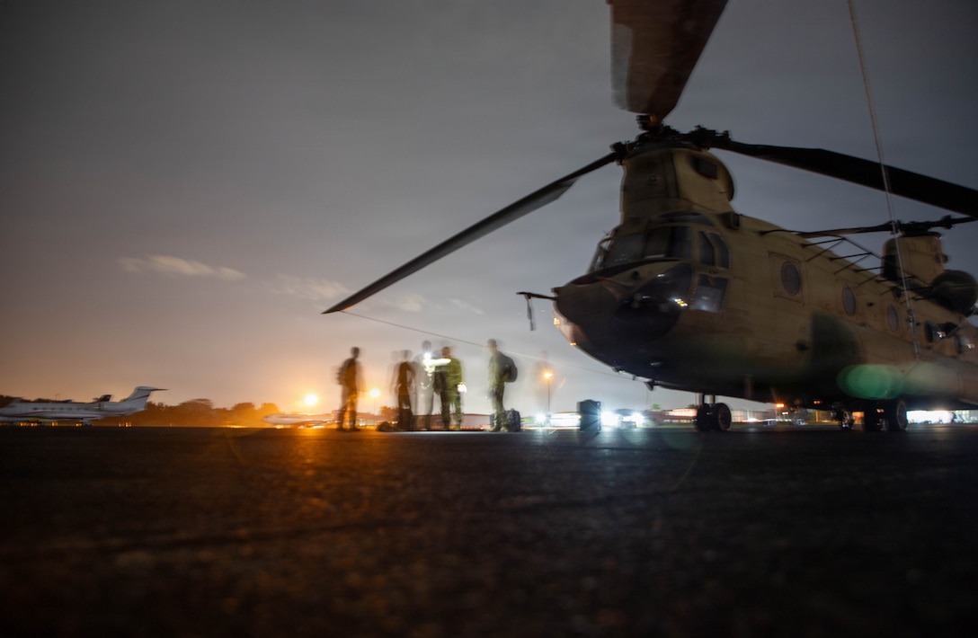 A military helicopter sits on the flightline at night.