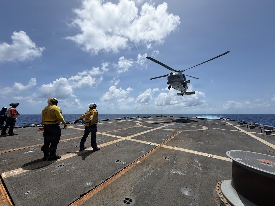 A military helicopter lands on the deck of a navy ship.