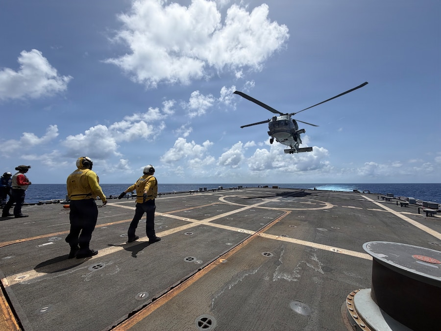 A military helicopter lands on the deck of a navy ship.