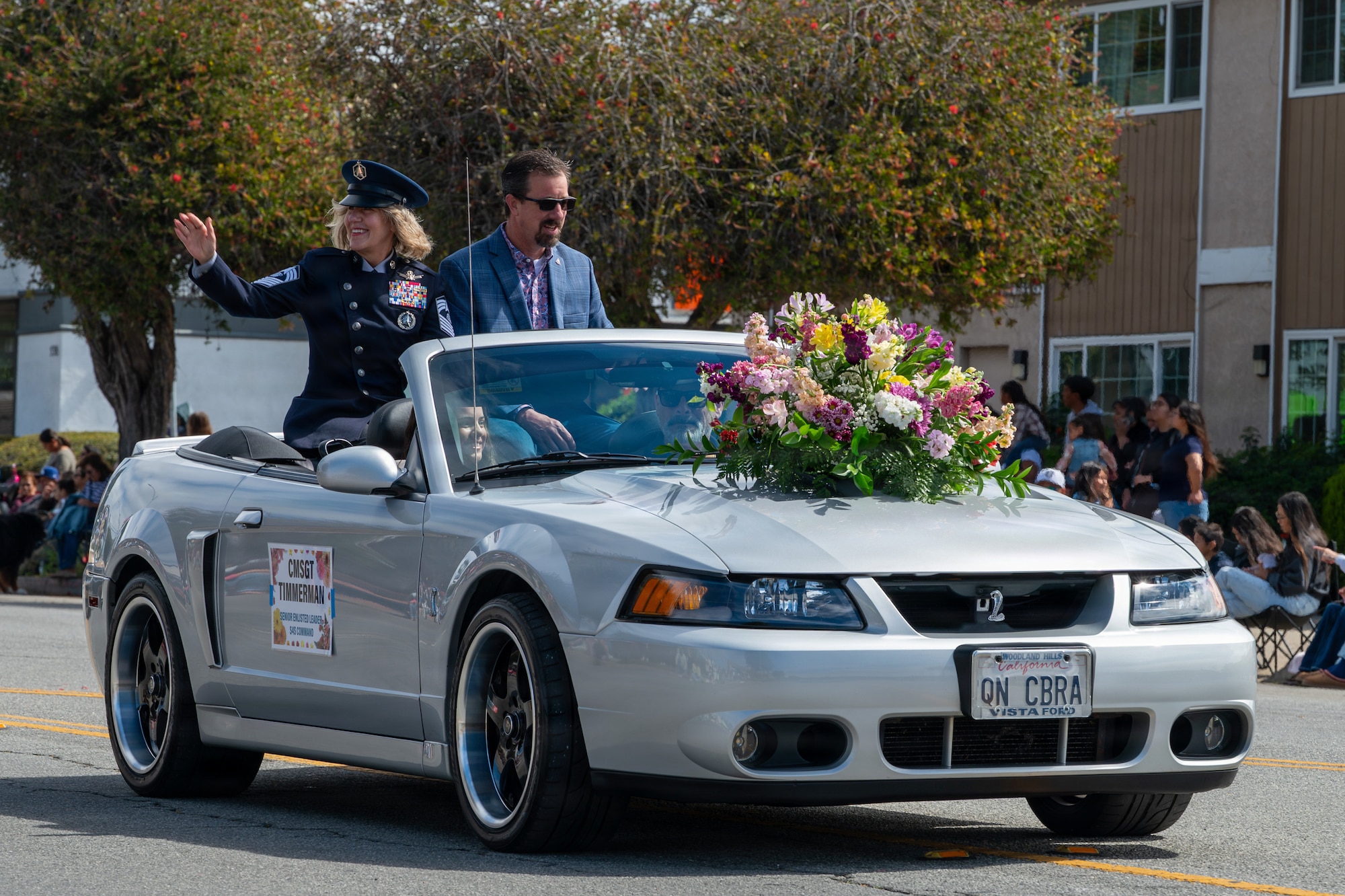 Two people sit in a car and wave at a crowd