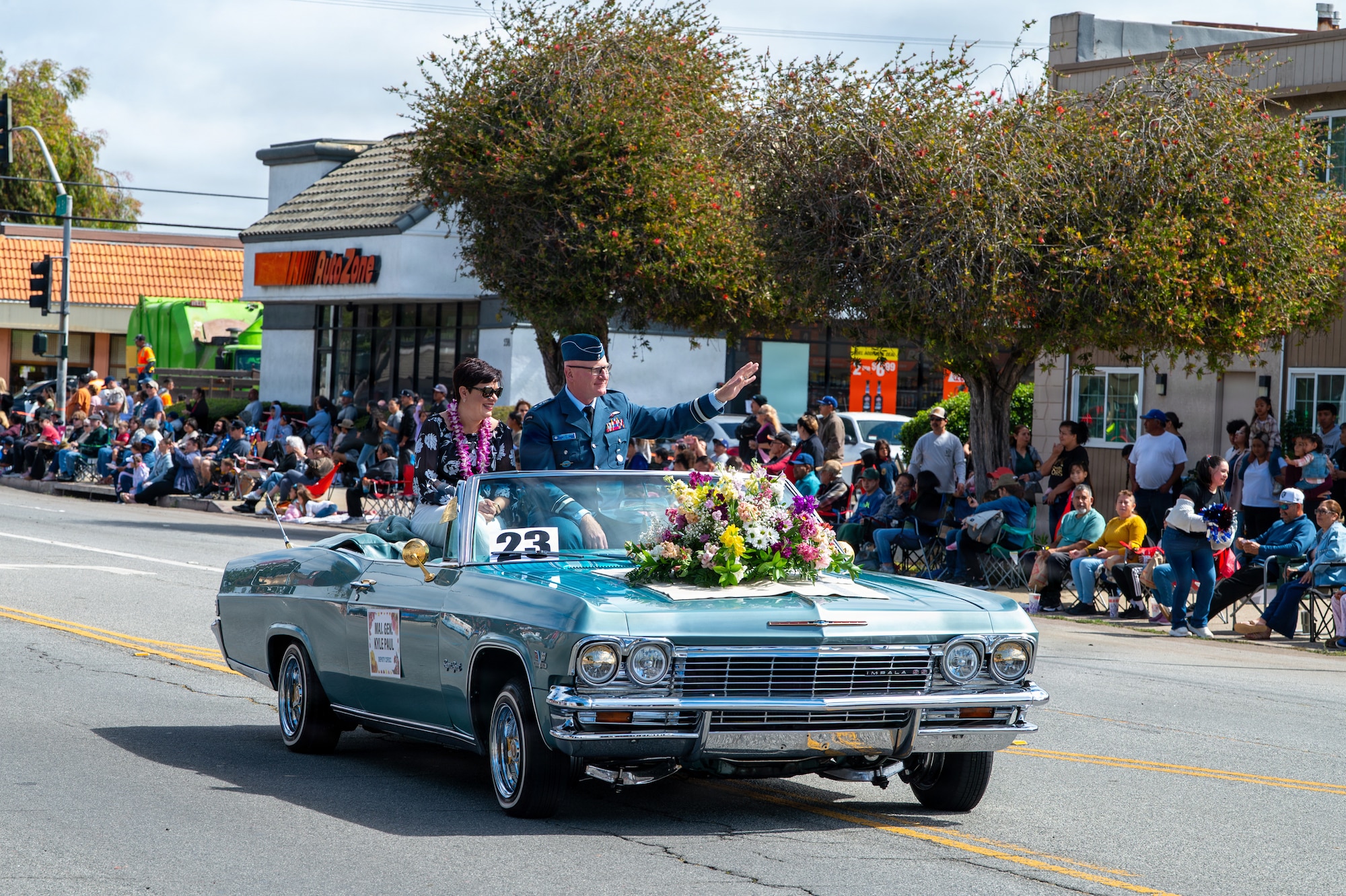 Two people sit in a car and wave at a crowd