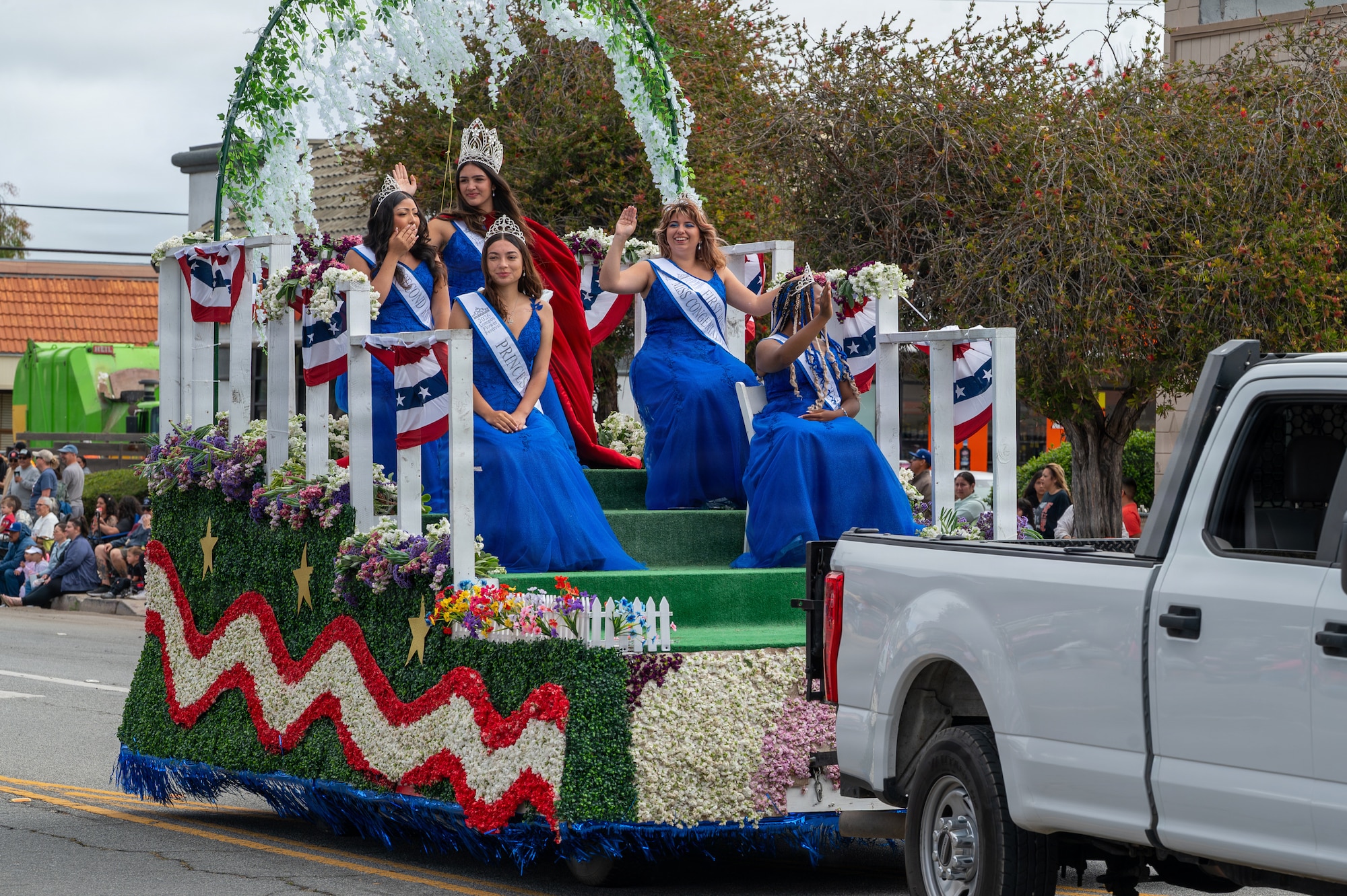 People sit on a parade float and wave to a crowd