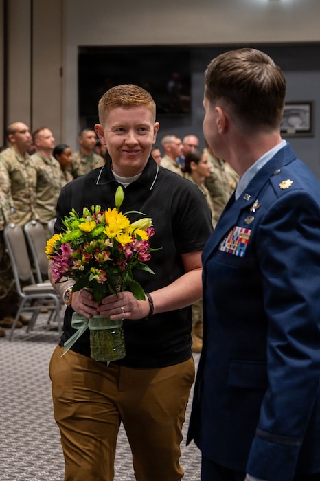 Two individuals look at each other, one holding a vase of flowers