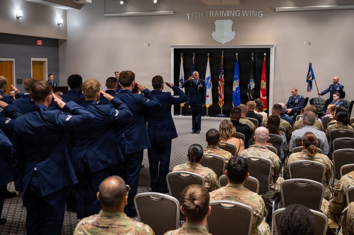 Service members in formation salute the service member in front of a crowd.