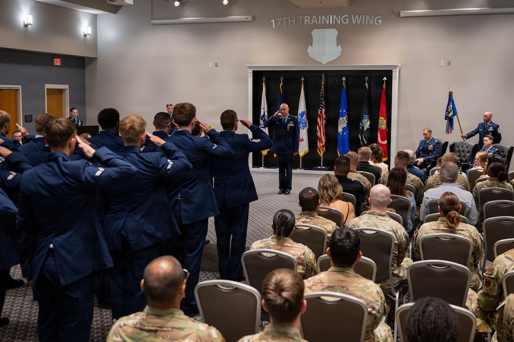 Service members in formation salute the service member in front of a crowd.