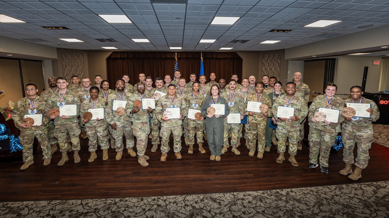 A group photo of men and women, wearing military camouflage uniforms, most wearing blue and white TSgt lanyards