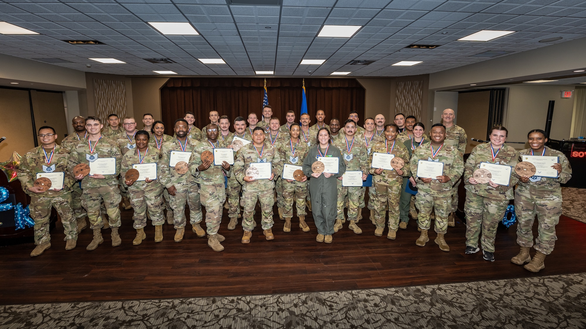 A group photo of men and women, wearing military camouflage uniforms, most wearing blue and white TSgt lanyards