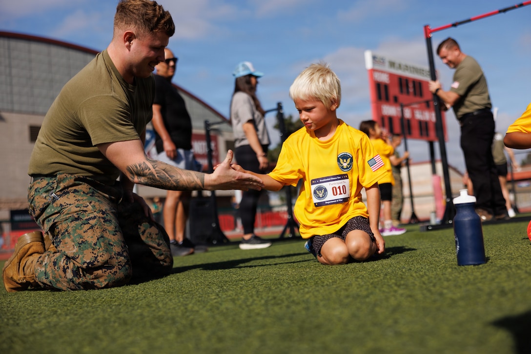 A child shakes the hand of a U.S. Marine after finishing the plank during the Presidential Fitness Test at Marine Corps Base Camp Pendleton, Calif., June 26, 2026. The Presidential Fitness Test is a national youth fitness assessment designed to promote strength, endurance, cardiovascular health and overall physical well-being by providing a standardized way for young people to measure their performance. (U.S. Marine Corps photo by Pfc. Joseph Cantu.)
