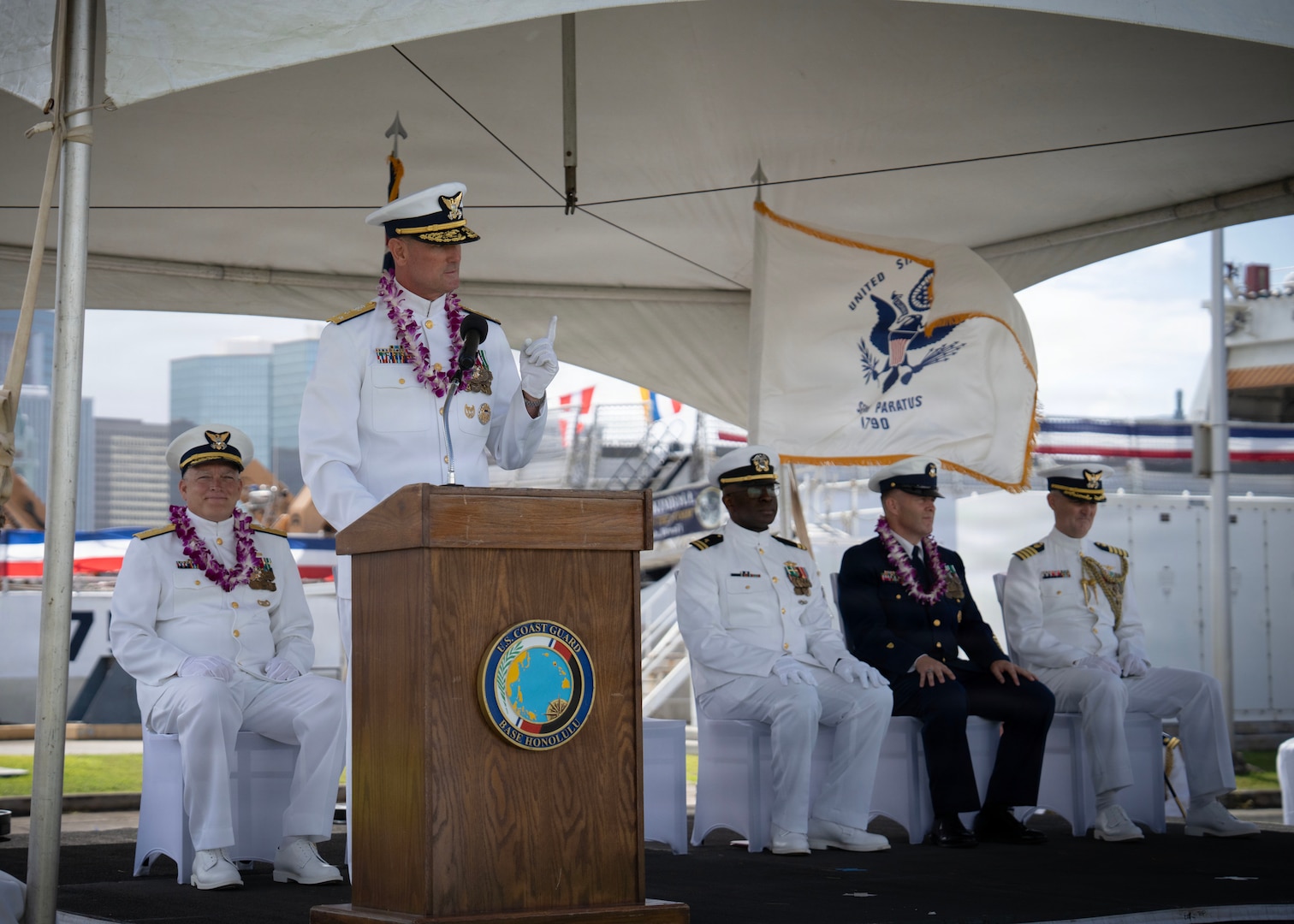 Vice Adm. Buzzella speaks to a crowd. There are officers and enlisted behind him.