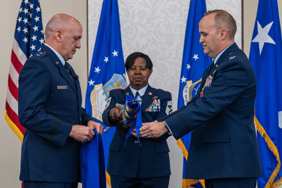 3 individuals stand on stage as the cover a unit guidon.