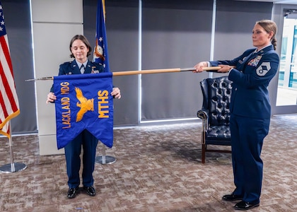 U.S. Air Force Col. Shawn Garcia, commander of the Lackland Medical Group, and Chief Master Sgt. Codi Bowman, senior enlisted leader of the Lackland Mental Health Squadron, unfurl the squadron guidon during the unit's activation ceremony at Wilford Hall Ambulatory Surgical Center, Joint Base San Antonio-Lackland, Texas, June 25, 2026.