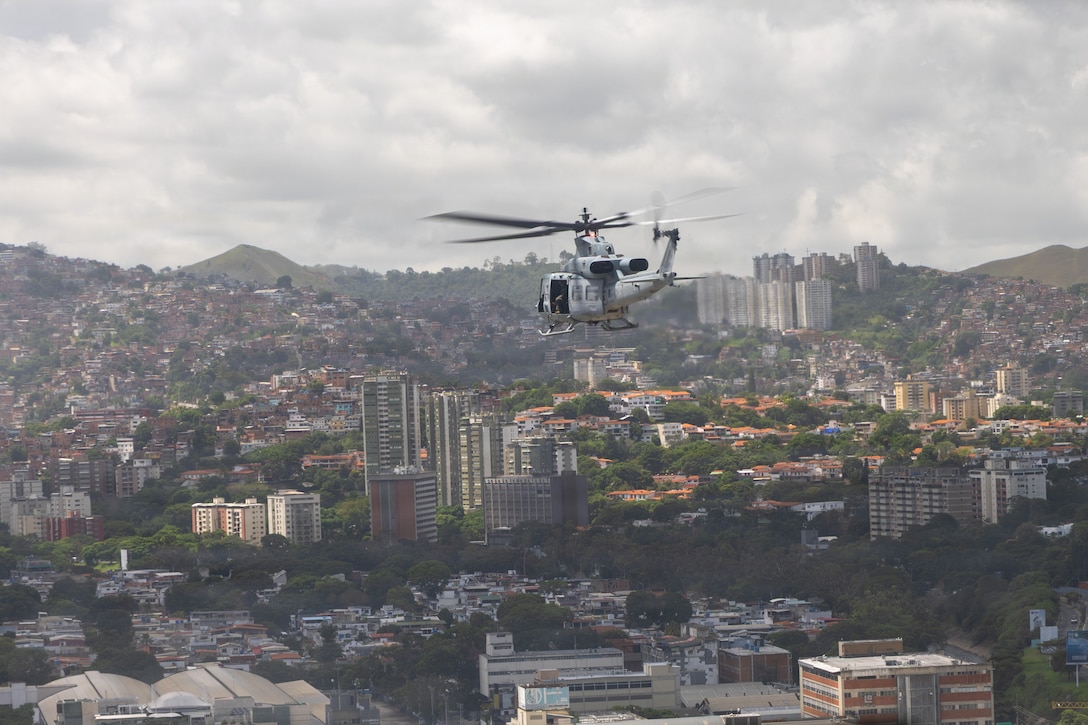 A military helicopter in flight over a city.
