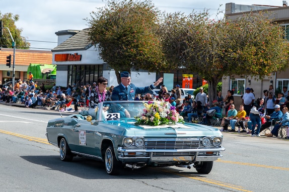 Two people sit in a car and wave at a crowd