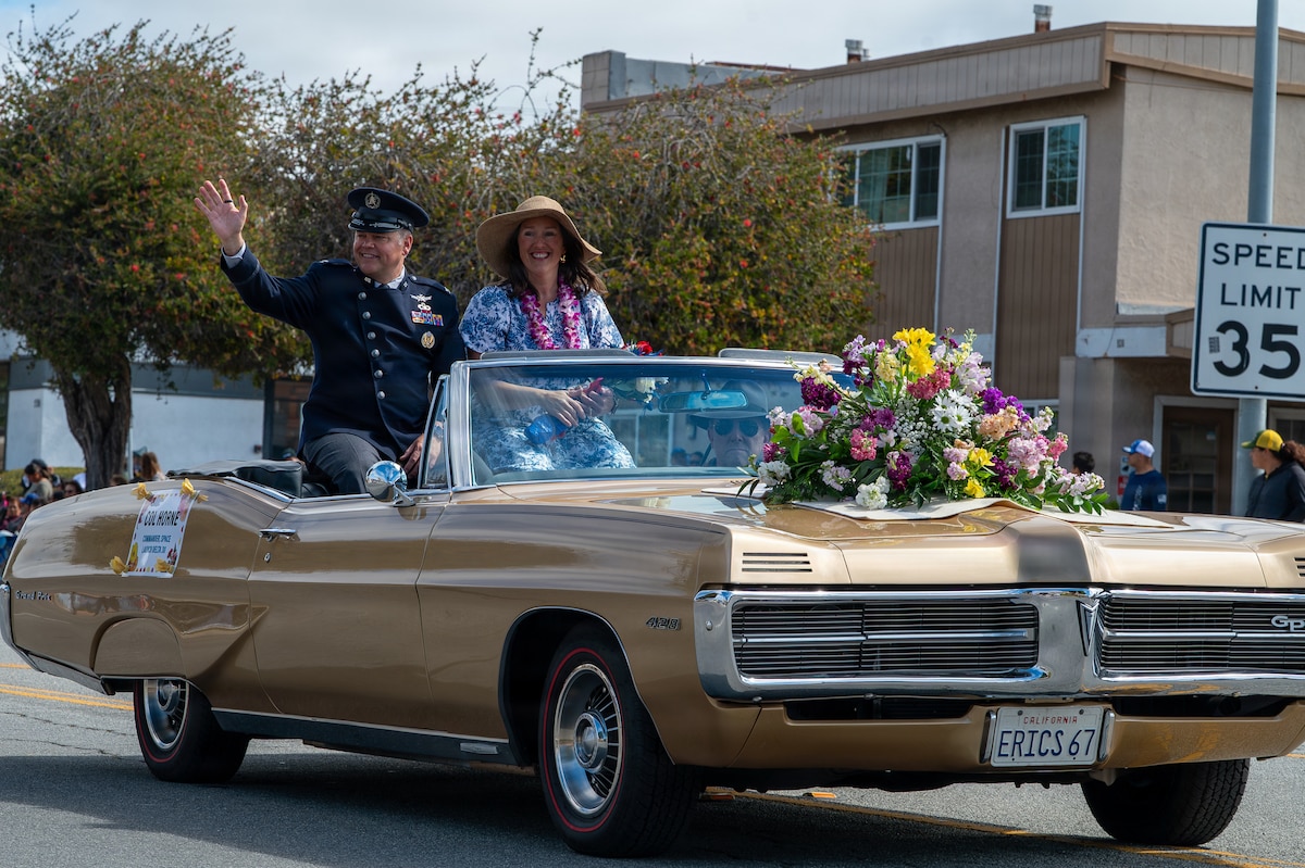 Two people sit in a car and wave at a crowd