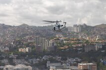 A military helicopter in flight over a city.