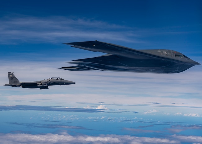 A fighter jet and stealth bomber fly together