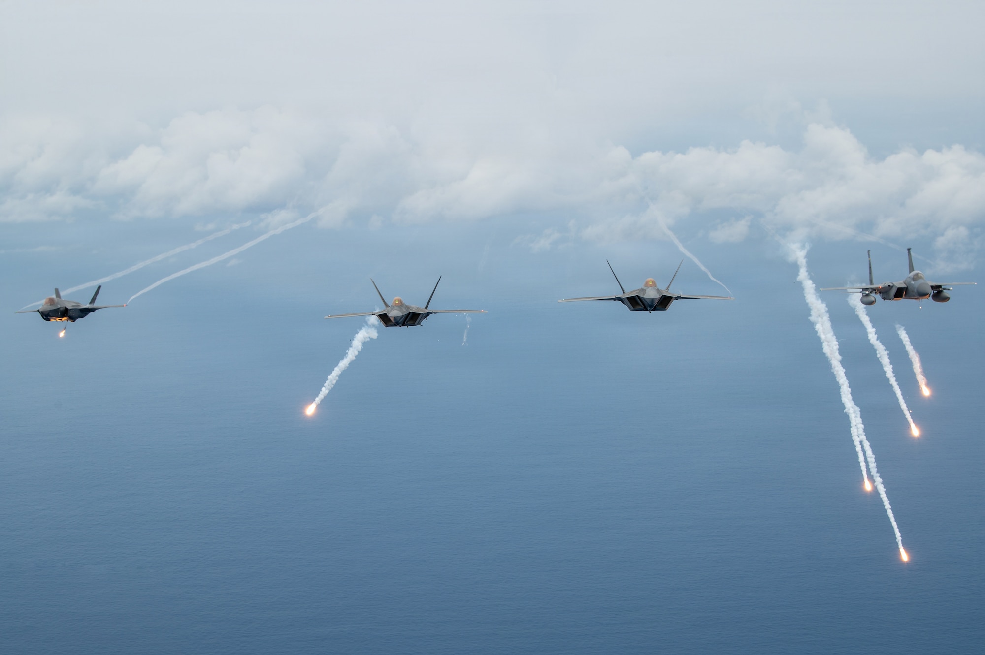 A U.S. Air Force F-35A Lightning II aircraft assigned to the 115th Fighter Wing, Wisconsin Air National Guard, U.S. Air Force F-22 Raptor aircraft assigned to the 199th Fighter Squadron, Hawaii Air National Guard, and a U.S. Air Force F-15C/D Eagle aircraft, assigned to the 159th Fighter Wing, Louisiana Air National Guard, let off flares during exercise Sentry Aloha 26-1, over the Pacific Ocean, Jan. 20, 2026. Sentry Aloha is built around Dissimilar Air Combat Training, which challenges pilots to engage in combat scenarios against aircraft with different performance capabilities. (U.S. Air National Guard photo by Master Sgt. Mary Greenwood)
