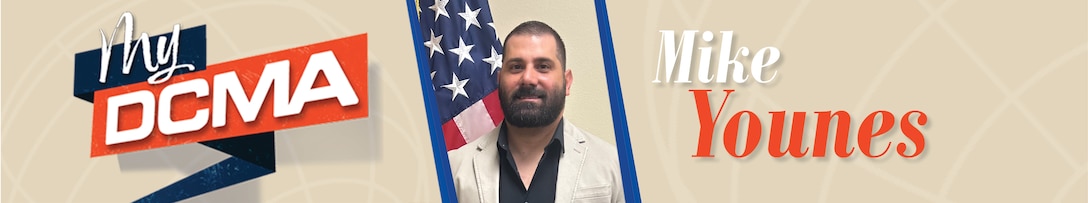 Smiling man with a beard wears a black shirt and stands near the American flag