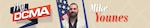 Smiling man with a beard wears a black shirt and stands near the American flag