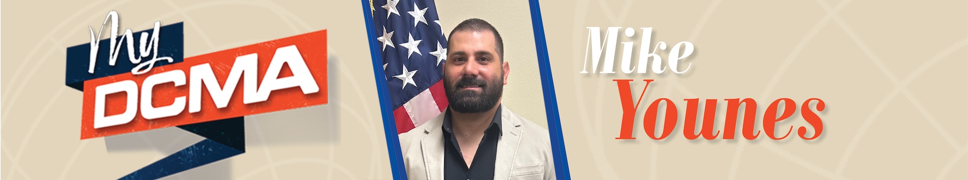 Smiling man with a beard wears a black shirt and stands near the American flag
