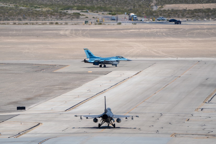 Two military jets taxi on a flight line.