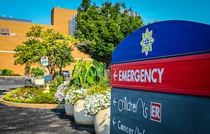 Blue sign and red sign. Emergency in white with red background pointing in the direction of the emergency department.