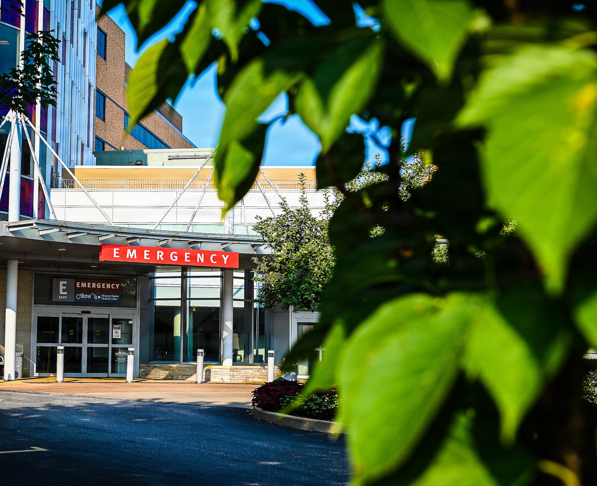 Green leaves in the forefront in the background the entrance to Missouri Baptist Medical Center emergency room.