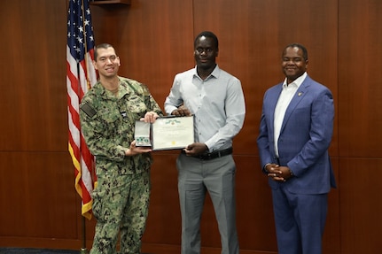 Naval Surface Warfare Center, Philadelphia Division (NSWCPD) Commanding Officer Capt. Ashley Wright and Technical Director Nigel C. Thijs, SES, present Electrical Engineer Maboury Gueye with the Department of the Navy Civilian Service Commendation Medal during NSWCPD’s Fiscal Year 2026 Third Quarter Awards Ceremony held June 17, 2026. Gueye was recognized for superior performance while serving as a subject matter expert providing urgent Support Equipment and Aircraft Launch and Recovery Equipment fleet support in a critical, forward-deployed environment. (U.S. Navy photo by Jay Butterbaugh, CTR)