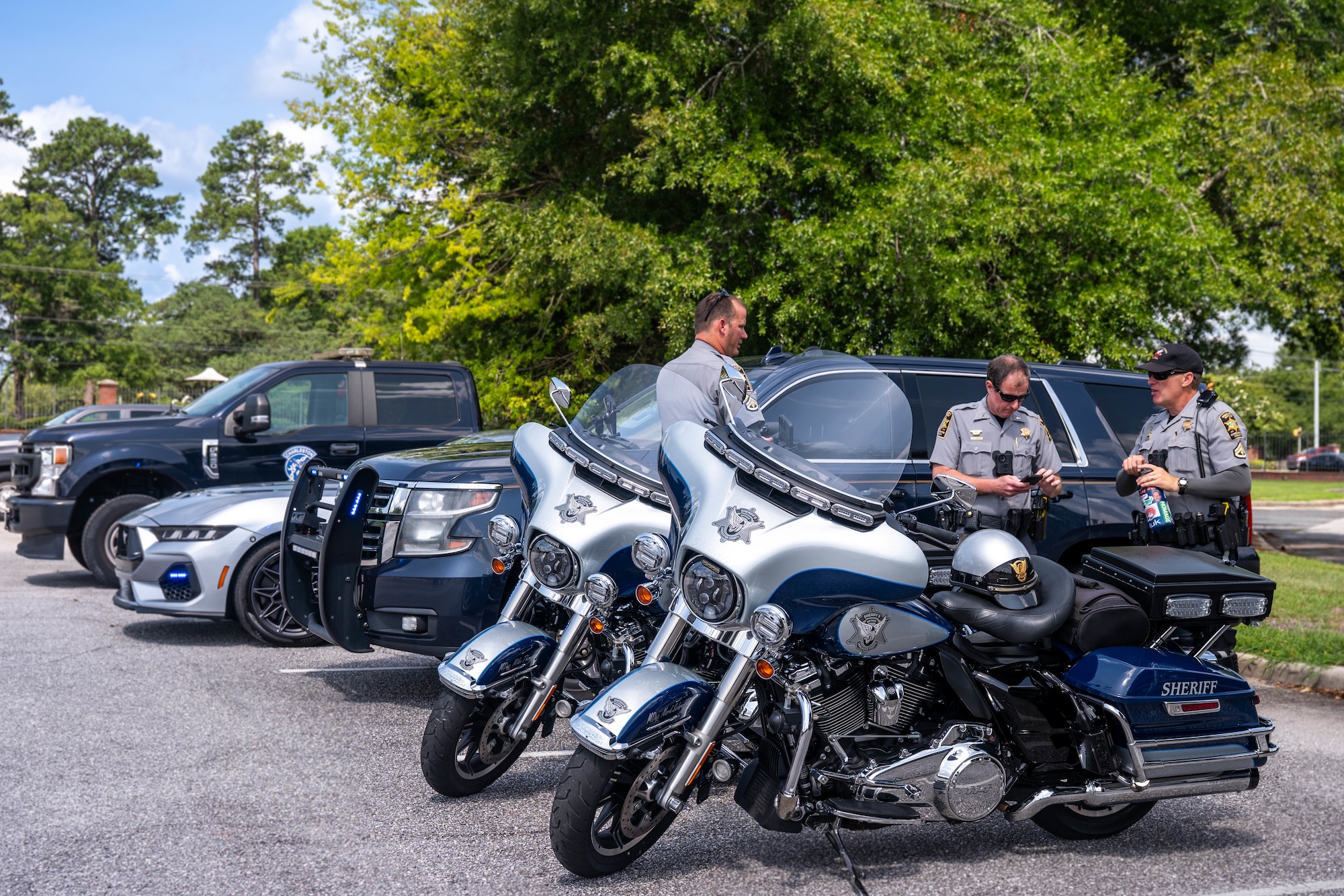 A photo of three police officers standing alongside their collection of patrol vehicles.