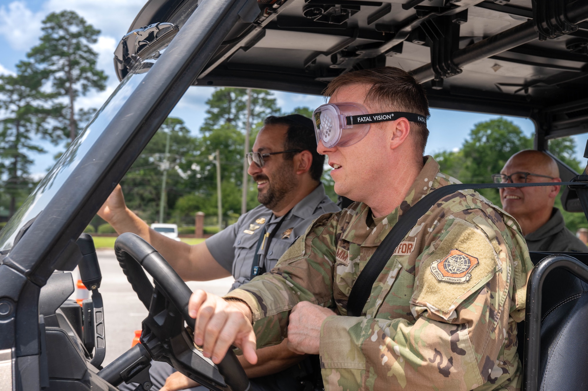 A photo of three people driving a Polaris XP 1000 through an outdoor obstacle course.