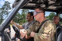 A photo of three people driving a Polaris XP 1000 through an outdoor obstacle course.