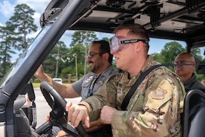 A photo of three people driving a Polaris XP 1000 through an outdoor obstacle course.