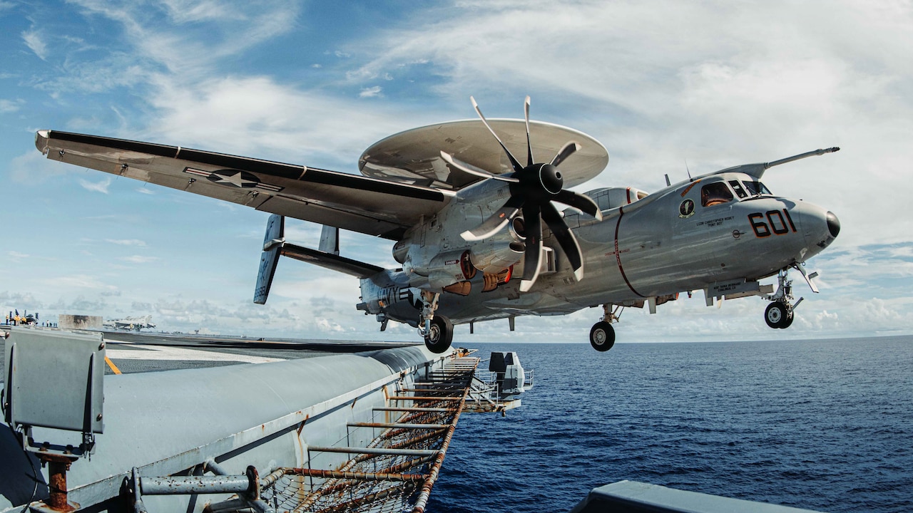 A military aircraft flies off the end of an aircraft carrier sailing in the ocean.