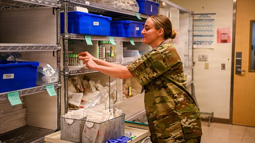 An Arimen in camouflage scrubs takes vials out of a package in a supply room.