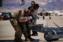 Three U.S. Air Force weapons load crew members assigned to the 57th Aircraft Maintenance Squadron prepare to load an inert air-to-air missile onto an F-16C Fighting Falcon during exercise VENOM FORGE at Creech Air Force Base, Nevada, June 17, 2026. Being close to Nellis AFB, Creech AFB provided realism and operational value to support a controlled hub-to-spoke training model, while allowing students to learn how to coordinate with a real host base. (U.S. Air Force photo by Staff Sgt. Jake Jacobsen)