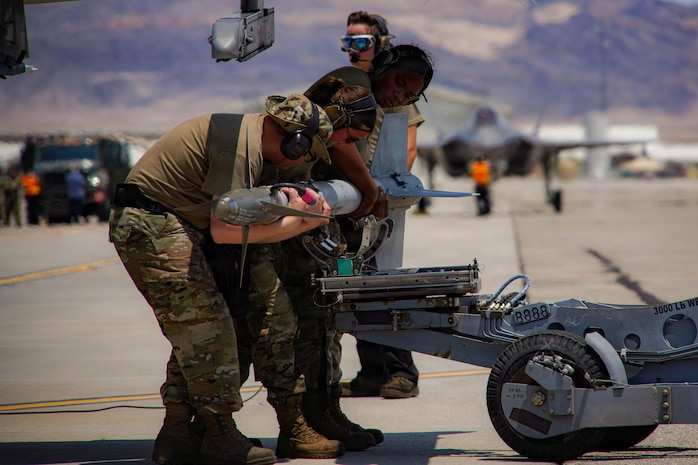 Three U.S. Air Force weapons load crew members assigned to the 57th Aircraft Maintenance Squadron prepare to load an inert air-to-air missile onto an F-16C Fighting Falcon during exercise VENOM FORGE at Creech Air Force Base, Nevada, June 17, 2026. Being close to Nellis AFB, Creech AFB provided realism and operational value to support a controlled hub-to-spoke training model, while allowing students to learn how to coordinate with a real host base. (U.S. Air Force photo by Staff Sgt. Jake Jacobsen)