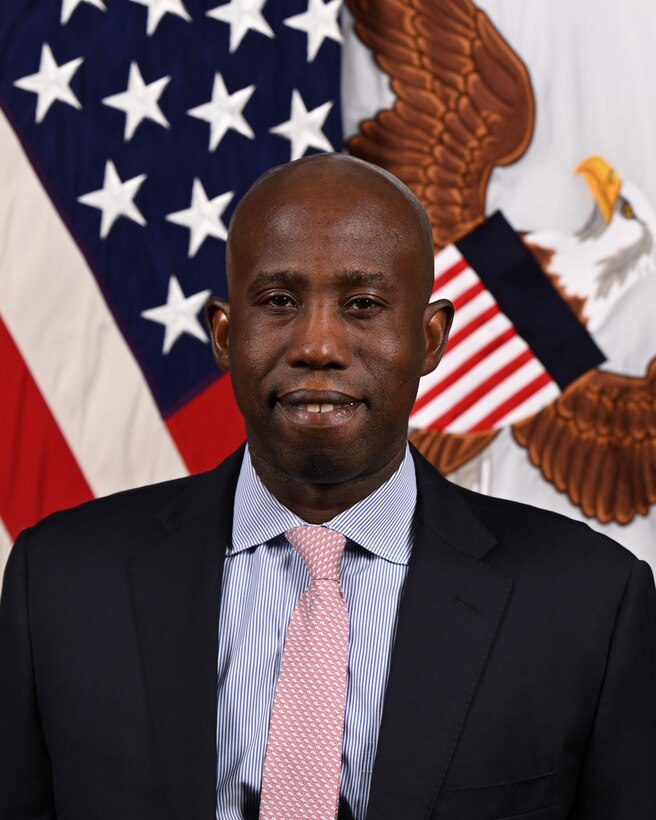 Person poses for official photo in front of U.S. and General council flags behind.