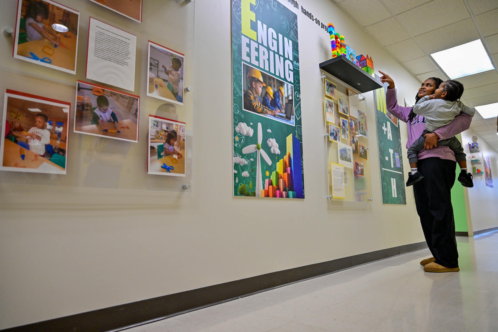 A teacher at the DSCR CDC shows a child the engineering display on the STEM wall, an addition made during a recent upgrade to the center.