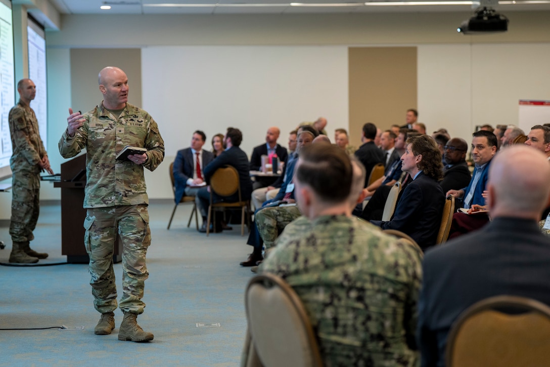 A soldier stands and talks to a seated audience.