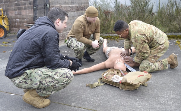 chest seal scrutiny… Under the watchful gaze of Navy Medicine Readiness Training Command Bremerton Tactical Combat Casualty Care instructors, 315th Aeromedical Evacuation Squadron personnel hone their medical response skills in treating traumatic injuries on the field of battle. The visiting Air Force personnel from Charleston Air Force Base, South Carolina, received intensive didactic module training before undergoing and completing their educational effort with actual hands-on application in the field. Amidst a mock firefight exploding around them, faux patient screams and bellowing demands from instructors, the 315th team were tested on conducting – with timely urgency - primary and secondary assessments, casualty movement, airway management, hemorrhage control, chest needle decompression, applying splinting and pressure dressings, and more (Official Navy photo by Douglas H Stutz, NHB/NMRTC Bremerton public affairs officer).