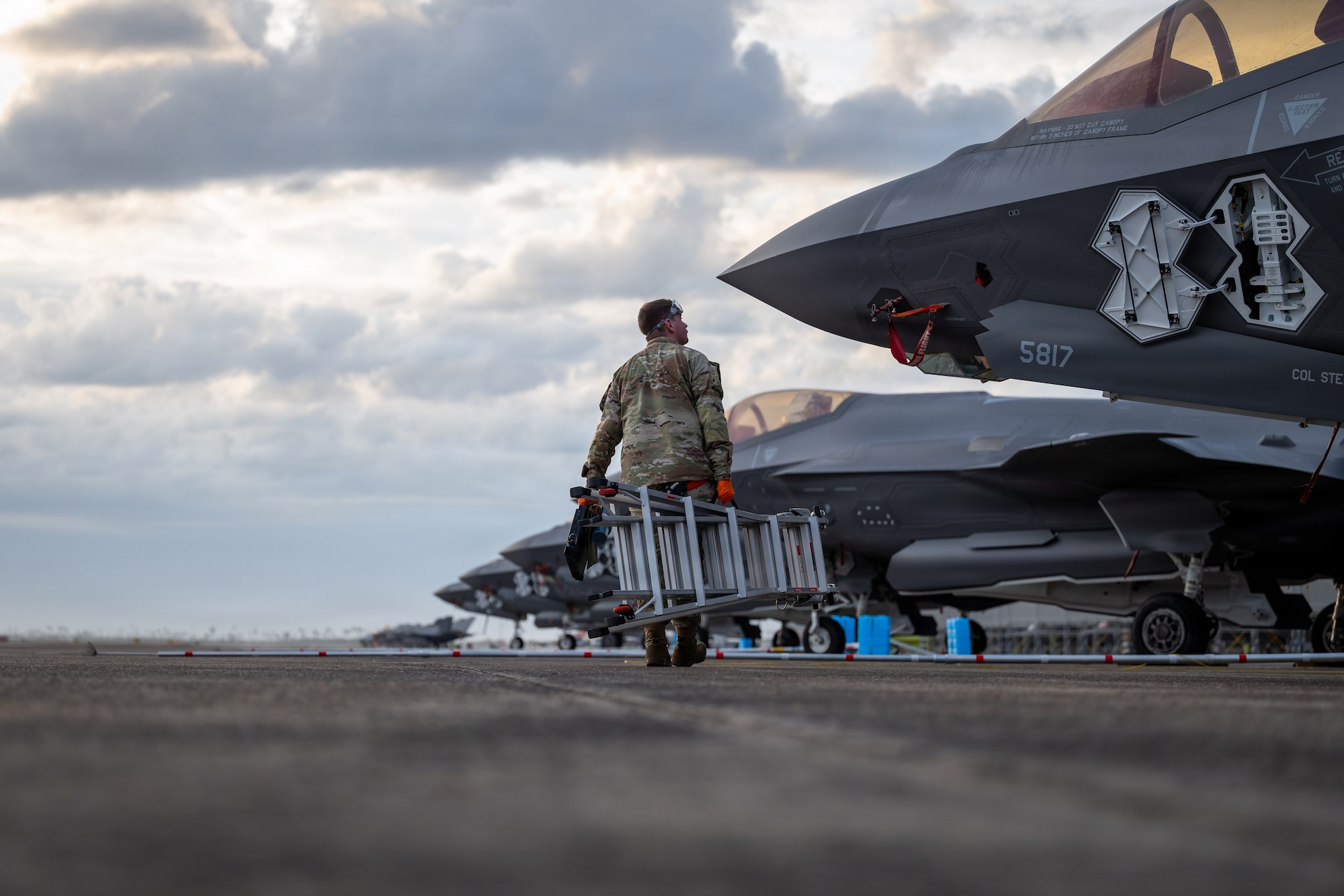 An Airman looks up at a F-35A Lightning II aircraft while carrying a ladder on a flightline at Tyndall Air Force Base, Florida.