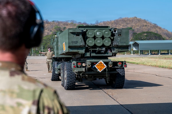 U.S. Airman 1st Class Jamie Carden, a 39th Airlift Squadron load master, serves as a ground guide while directing an M142 High Mobility Artillery Rocket System (HIMARS) onto a U.S. Air Force C-130J Super Hercules in preparation of a High Mobility Artillery Rocket System Rapid Infiltration (HIRAIN) training during Exercise Cobra Gold 2026 at Lopburi, Thailand, March 1, 2026.