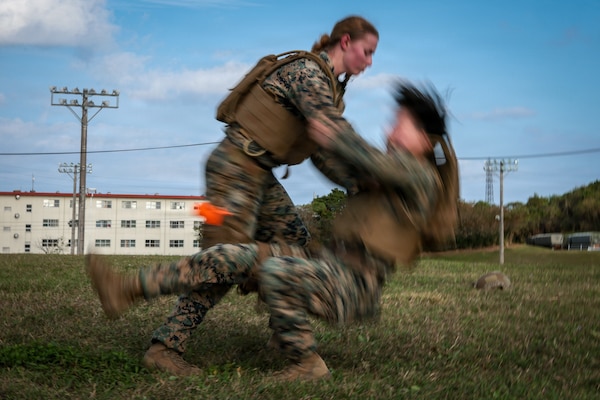 U.S. Marine Corps 2nd Lt. Kyra Norton, left, a native of Florida and a logistics officer, performs a leg sweep on Sgt. Marie Abe, a native of California and an influence specialist, both with 5th Air Naval Gunfire Liaison Company, III Marine Expeditionary Force Information Group, during a Marine Corps Martial Arts Program black belt culminating event at Camp Hansen, Okinawa, Japan, Feb. 26, 2026.