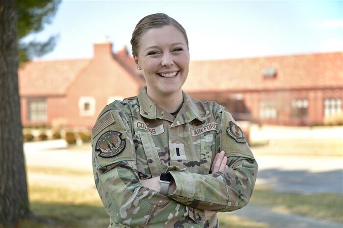 A woman in an occupational camouflage uniform stands outside and smiles for a photo